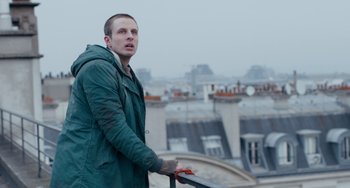 Movie still from “The Night Eats the World” (2018), directed by Dominique Rocher – A man standing on top of a building looking over the rooftops; Medium shot, Low angle