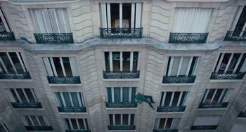 Movie still from “The Night Eats the World” (2018), directed by Dominique Rocher – A man is climbing up the side of a tall building; Extreme Wide shot, Overhead angle