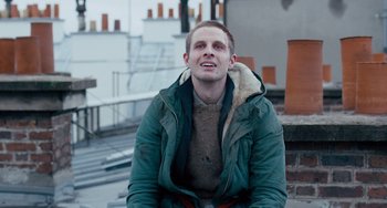 Movie still from “The Night Eats the World” (2018), directed by Dominique Rocher – A man sitting on the ground wearing a jacket; Close Up shot, Low angle