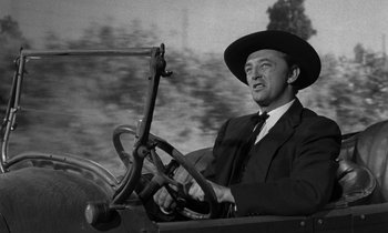 Movie still from “The Night of the Hunter” (1955), directed by Charles Laughton – A man in a suit and hat driving a car; Close Up shot, Low angle