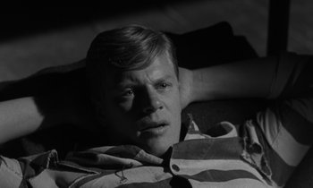 Movie still from “The Night of the Hunter” (1955), directed by Charles Laughton – A black and white photo of a man laying on a bed; Close Up shot, High angle