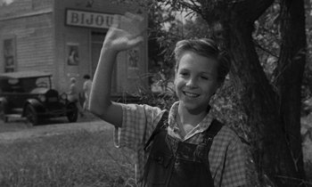 Movie still from “The Night of the Hunter” (1955), directed by Charles Laughton – A young boy waving at the camera in a black and white photo; Medium shot, Over the shoulder angle