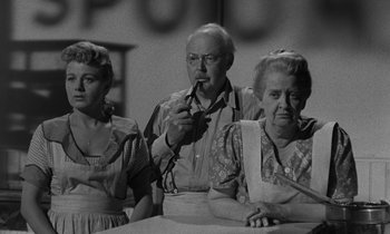 Movie still from “The Night of the Hunter” (1955), directed by Charles Laughton – A man and two women sitting in front of a table; Medium shot, Low angle