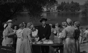 Movie still from “The Night of the Hunter” (1955), directed by Charles Laughton – A group of people standing around a table; Medium shot, Over the shoulder angle