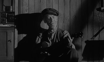 Movie still from “The Night of the Hunter” (1955), directed by Charles Laughton – An older man sitting in a chair holding a ukulele; Medium shot, Low angle