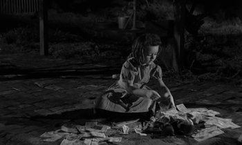 Movie still from “The Night of the Hunter” (1955), directed by Charles Laughton – A little girl sitting on the ground playing with papers; Medium shot, High angle