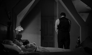 Movie still from “The Night of the Hunter” (1955), directed by Charles Laughton – A man standing next to a bed in a room; Wide shot, High angle