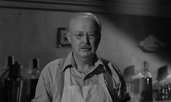 Movie still from “The Night of the Hunter” (1955), directed by Charles Laughton – An older man wearing an apron and glasses in a kitchen; Close Up shot, Low angle