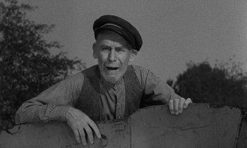 Movie still from “The Night of the Hunter” (1955), directed by Charles Laughton – An old man wearing a hat is leaning on a fence; Medium shot, Low angle