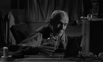 Movie still from “The Night of the Hunter” (1955), directed by Charles Laughton – An older man sitting at a table with a glass of wine; Medium shot, Low angle