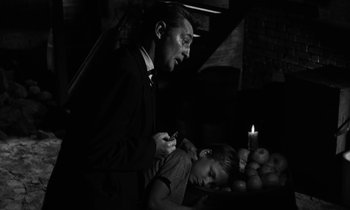 Movie still from “The Night of the Hunter” (1955), directed by Charles Laughton – A man and a boy in a dark room with a candle; Medium shot, Over the shoulder angle
