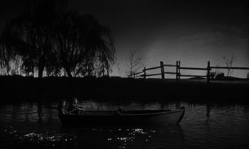 Movie still from “The Night of the Hunter” (1955), directed by Charles Laughton – A person in a boat on a body of water at night; Wide shot, High angle