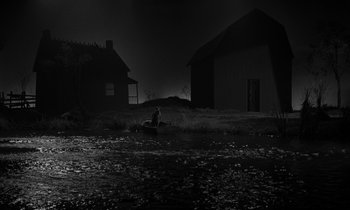 Movie still from “The Night of the Hunter” (1955), directed by Charles Laughton – A person sitting in a field near some houses; Extreme Wide shot, High angle