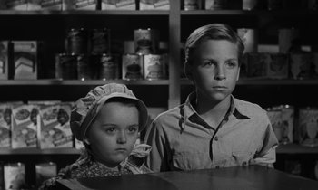 Movie still from “The Night of the Hunter” (1955), directed by Charles Laughton – A young boy and a young girl sitting at a table in front of a shelf; Close Up shot, Over the shoulder angle
