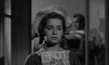 Movie still from “The Night of the Hunter” (1955), directed by Charles Laughton – A young woman wearing a straw hat and a movie poster; Close Up shot, Over the shoulder angle