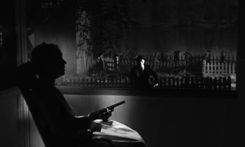 Movie still from “The Night of the Hunter” (1955), directed by Charles Laughton – A man sitting at a table in front of a bar holding a cell phone; Wide shot, Over the shoulder angle