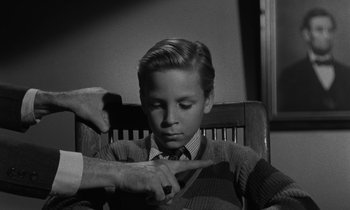 Movie still from “The Night of the Hunter” (1955), directed by Charles Laughton – A young boy sitting in a chair with an older man; Medium shot, High angle