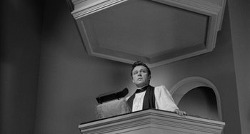 Movie still from “The Night of the Iguana” (1964), directed by John Huston – A man standing on top of a building with a microphone in front of him; Medium shot, Low angle