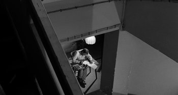 Movie still from “The Night of the Iguana” (1964), directed by John Huston – A man sitting on top of a stair railing; Wide shot, High angle