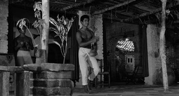 Movie still from “The Night of the Iguana” (1964), directed by John Huston – A man in white pants is holding a guitar in his hand; Wide shot, Low angle