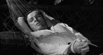 Movie still from “The Night of the Iguana” (1964), directed by John Huston – A black and white photo of a man laying in a hammock; Medium shot, High angle