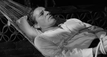Movie still from “The Night of the Iguana” (1964), directed by John Huston – A black and white photo of a man laying in a hammock; Medium shot, High angle