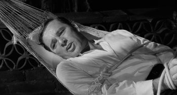 Movie still from “The Night of the Iguana” (1964), directed by John Huston – A black and white photo of a man laying in a hammock; Close Up shot, High angle