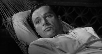 Movie still from “The Night of the Iguana” (1964), directed by John Huston – A black and white photo of a man laying in a bed; Close Up shot, High angle