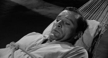 Movie still from “The Night of the Iguana” (1964), directed by John Huston – A black and white photo of a man laying in bed; Close Up shot, High angle