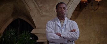 Movie still from “The Ninth Configuration” (1980), directed by William Peter Blatty – A man standing with his arms crossed in front of an archway; Medium shot, Low angle