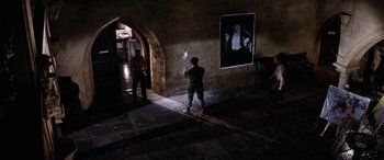 Movie still from “The Ninth Configuration” (1980), directed by William Peter Blatty – A man standing next to a wall with a painting on the wall; Wide shot, High angle