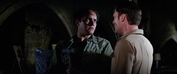Movie still from “The Ninth Configuration” (1980), directed by William Peter Blatty – A man in a green shirt is talking to another man in a brown shirt; Close Up shot, Over the shoulder angle