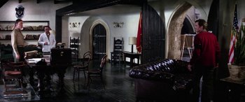 Movie still from “The Ninth Configuration” (1980), directed by William Peter Blatty – A living room filled with furniture next to a door way; Wide shot, High angle