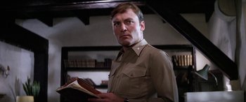 Movie still from “The Ninth Configuration” (1980), directed by William Peter Blatty – A man holding a book while wearing a uniform; Close Up shot, Low angle