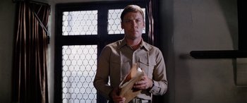 Movie still from “The Ninth Configuration” (1980), directed by William Peter Blatty – A man holding a book in front of a window; Medium shot, Low angle