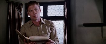 Movie still from “The Ninth Configuration” (1980), directed by William Peter Blatty – A man in a tan shirt holding a newspaper; Close Up shot, Low angle