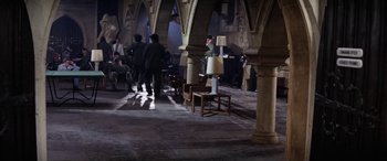 Movie still from “The Ninth Configuration” (1980), directed by William Peter Blatty – A group of people standing in a room with tables; Wide shot, High angle