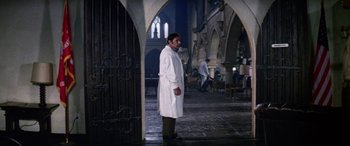 Movie still from “The Ninth Configuration” (1980), directed by William Peter Blatty – A man in a white lab coat standing in a building; Wide shot, Low angle