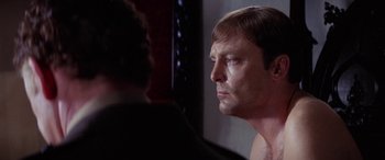 Movie still from “The Ninth Configuration” (1980), directed by William Peter Blatty – A person looking at his reflection in a mirror; Close Up shot, Over the shoulder angle