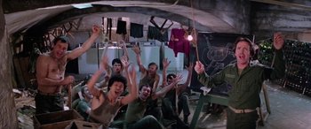 Movie still from “The Ninth Configuration” (1980), directed by William Peter Blatty – A group of people sitting in a room with their hands up; Wide shot, High angle