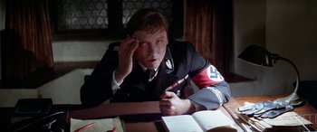 Movie still from “The Ninth Configuration” (1980), directed by William Peter Blatty – A man in a uniform sitting at a table with a book; Close Up shot, High angle