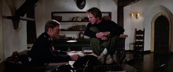 Movie still from “The Ninth Configuration” (1980), directed by William Peter Blatty – Two men are sitting at a table and talking to each other; Medium shot, Low angle