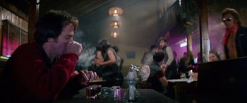 Movie still from “The Ninth Configuration” (1980), directed by William Peter Blatty – A group of people sitting at a table with drinks; Medium shot, Over the shoulder angle