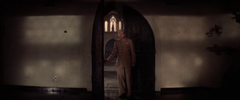 Movie still from “The Ninth Configuration” (1980), directed by William Peter Blatty – A man standing in front of an archway in a room; Wide shot, Low angle