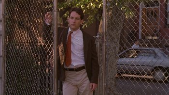 Movie still from “The Object of My Affection” (1998), directed by Nicholas Hytner – A man wearing a suit and tie standing in front of a fence; Medium shot, Low angle