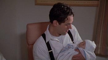 Movie still from “The Object of My Affection” (1998), directed by Nicholas Hytner – A man sitting in a chair holding a baby in his arms; Close Up shot, Over the shoulder angle