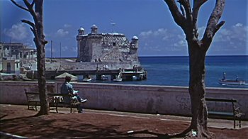 Movie still from “The Old Man and the Sea” (1958), directed by Fred Zinnemann – A man sitting on a bench looking out at the ocean; Extreme Wide shot, Low angle
