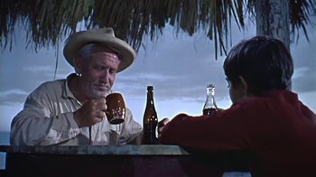 Movie still from “The Old Man and the Sea” (1958), directed by Fred Zinnemann – An old man sitting at a table with a bottle of beer; Medium shot, Low angle