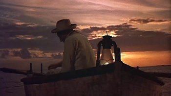 Movie still from “The Old Man and the Sea” (1958), directed by Fred Zinnemann – A man sitting on top of a boat at sunset; Wide shot, Low angle
