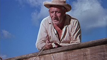Movie still from “The Old Man and the Sea” (1958), directed by Fred Zinnemann – An old man wearing a cowboy hat is leaning on a wall; Medium shot, Low angle